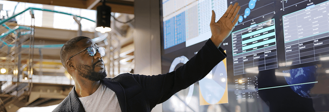 man conducting a seminar / lecture with the aid of a large screen. The screen is displaying graphs & data associated with movie clips of the earth.