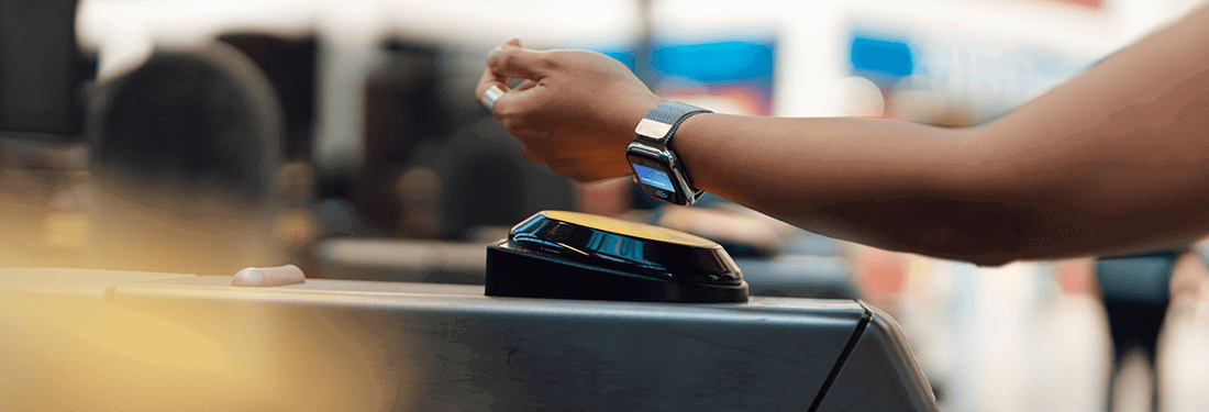 Cropped shot of young woman holding mobile device close to the payment terminal at the entrance of train station.